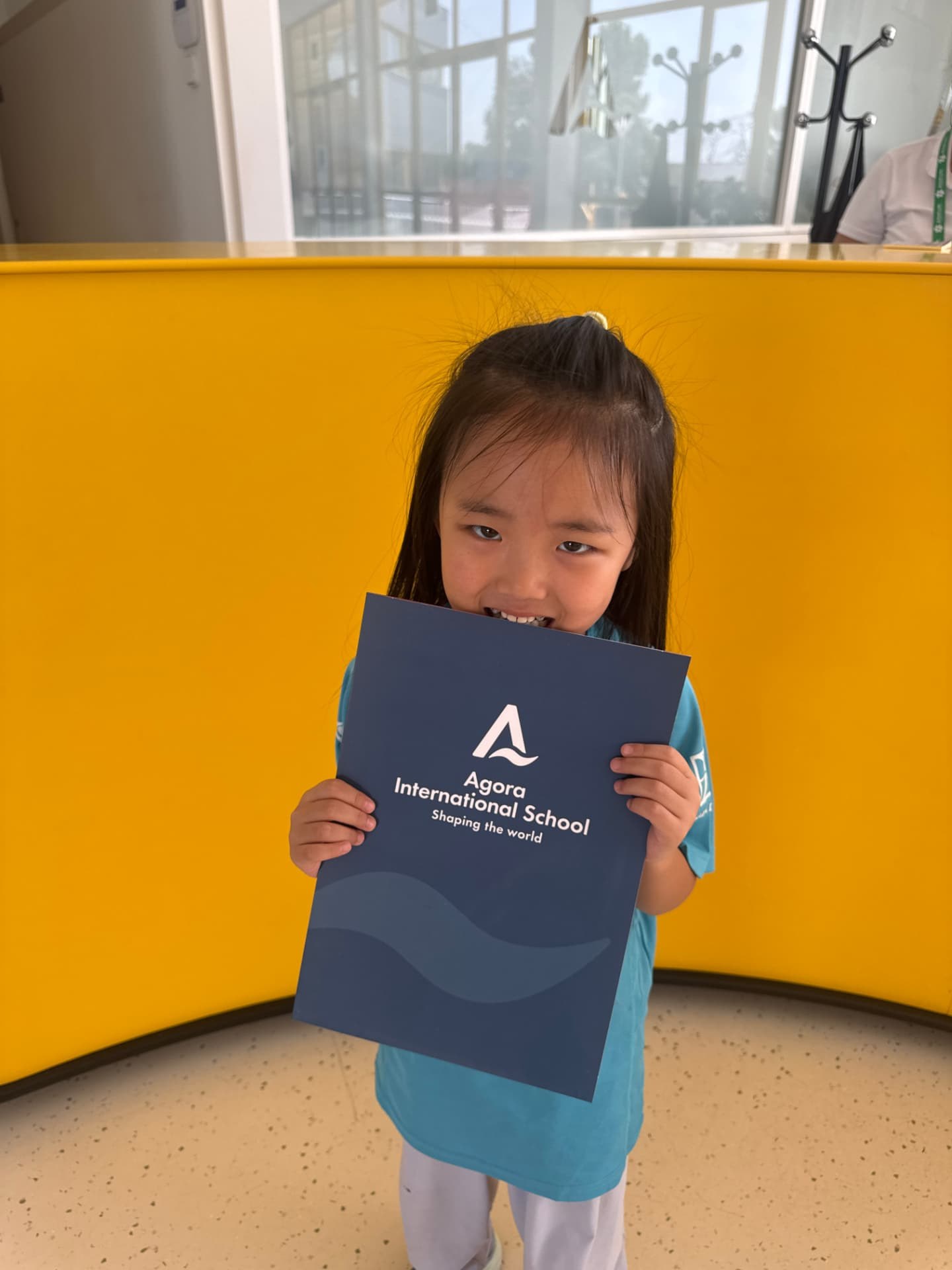 A smiling student holding an Agora International School folder